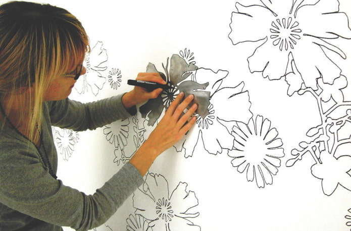 femme peignant des fleurs sur le mur à l'aide d'un pochoir